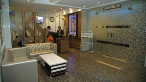 Un vestíbulo de hotel con una mesa de recepción, una zona de estar y un letrero de restaurante.