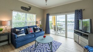 Un salon avec un canapé bleu, une table basse, un téléviseur et un balcon offrant une vue dégagée.