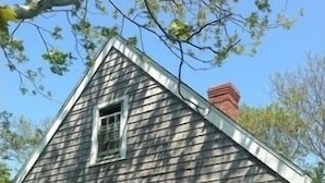 A two-story wooden house with a gabled roof and a chimney.