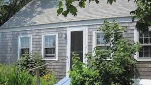 A house with a blue ramp leading to the front door, surrounded by greenery and a small garden.