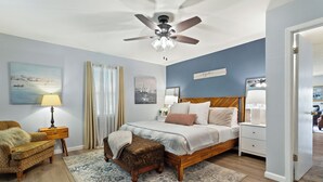 A bedroom with a bed, nightstands, a chair, a ceiling fan, and a view of the adjacent room.