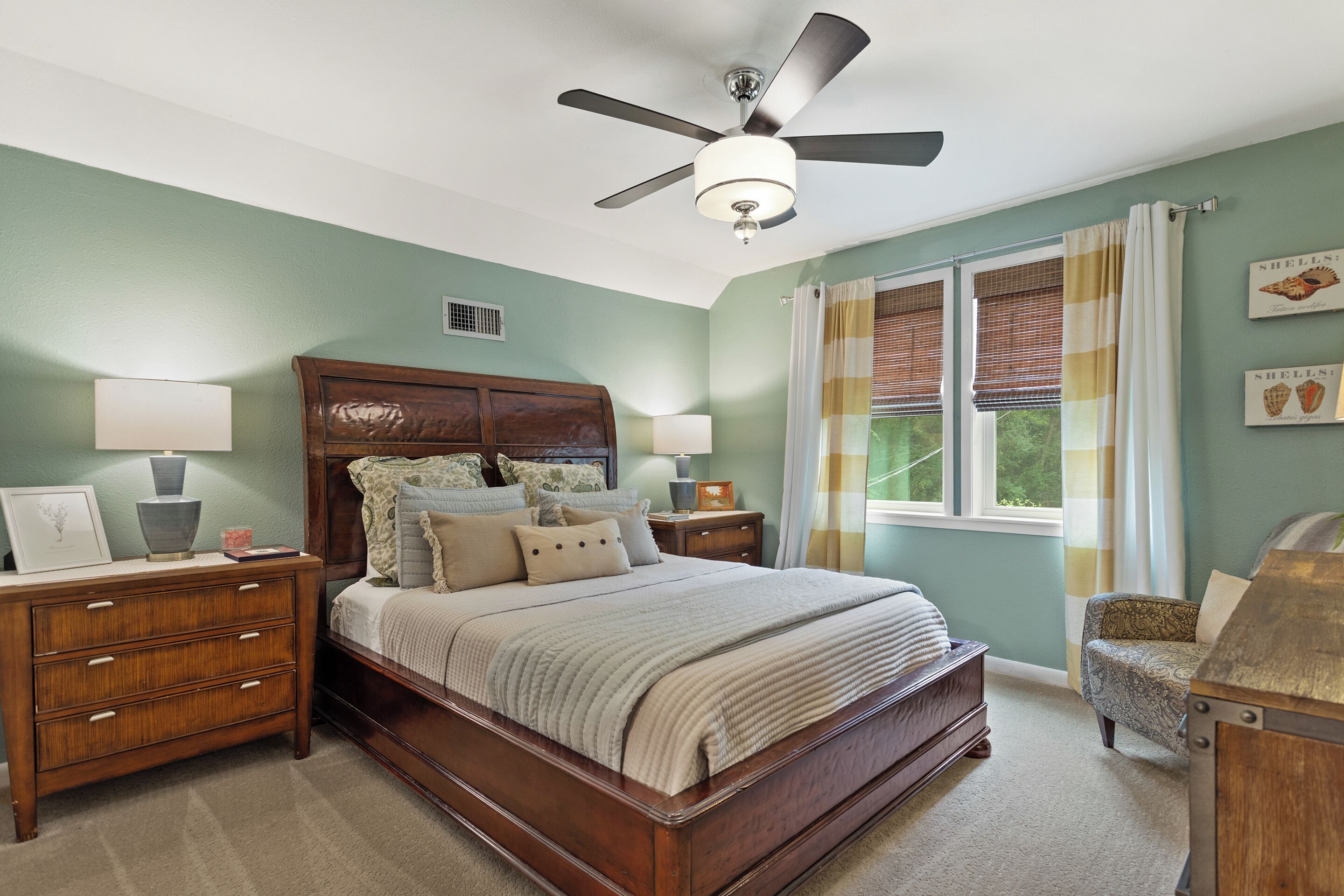 A bedroom with a wooden bed, nightstands, a ceiling fan, and a window with curtains.