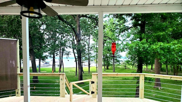 A wooden deck with a railing overlooking a grassy area with trees and a body of water.