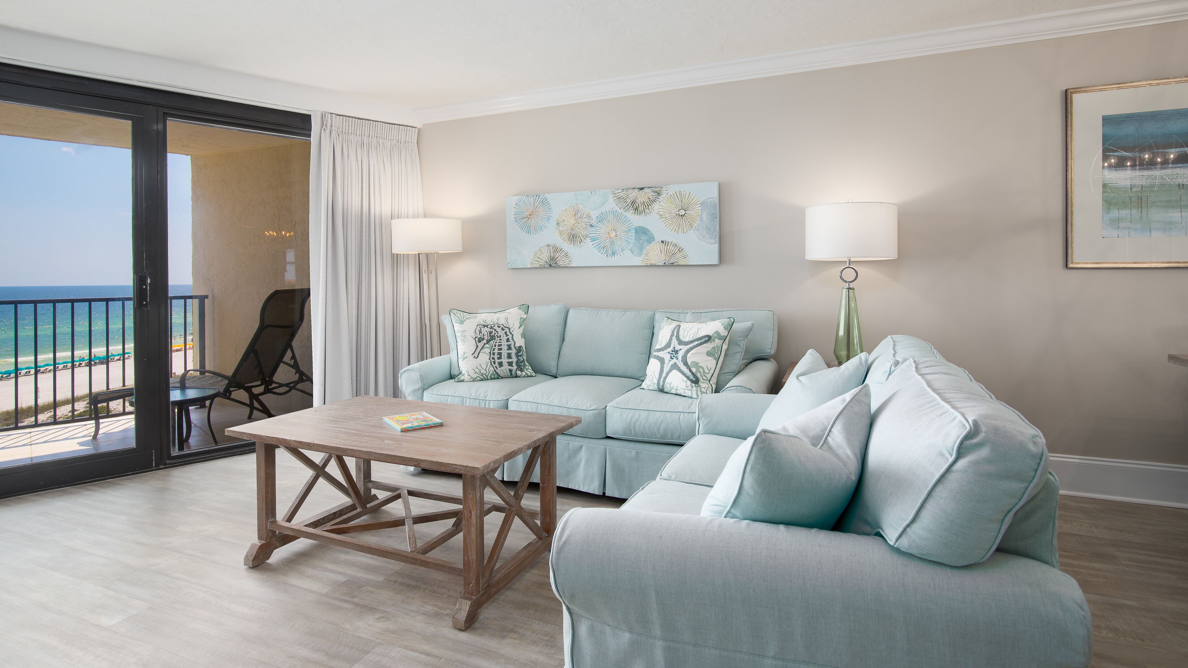 A living room with a sofa, a coffee table, and a view of the beach through a sliding door.