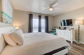Ein Schlafzimmer mit Bett, Kommode, Stuhl, Fernseher und Deckenventilator.