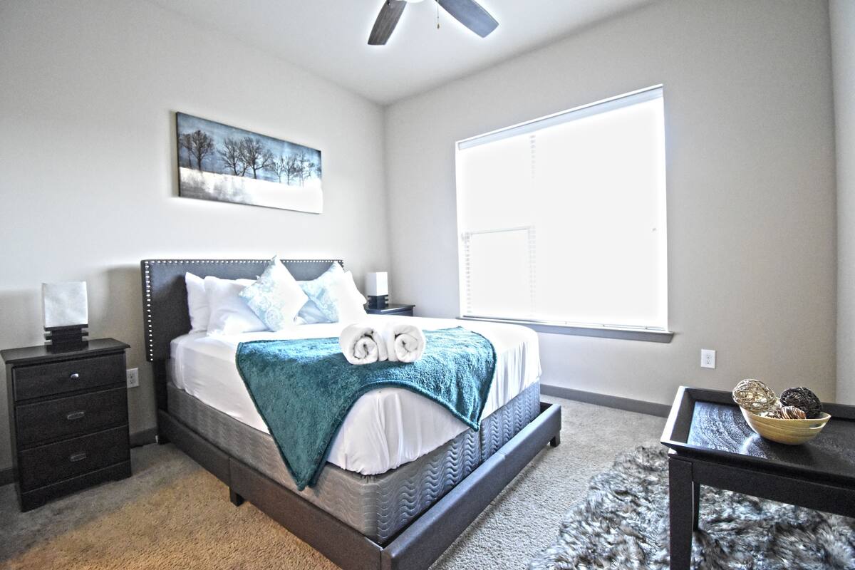 A bedroom with a bed, bedside tables, a window, and a painting on the wall.