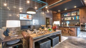 Una sala de estar moderna con chimenea, una mesa de centro de madera y una zona de bar con taburetes.