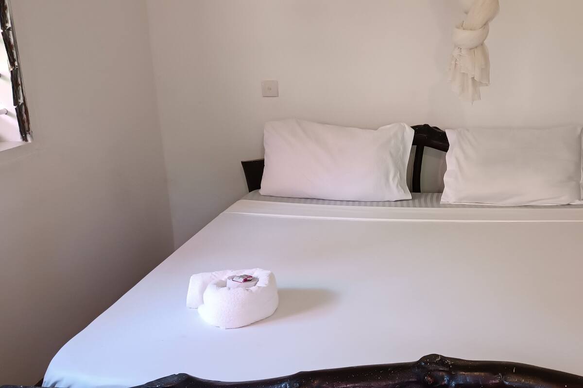 Una cama con ropa de cama blanca y dos almohadas, una toalla blanca y una lámpara de pared.