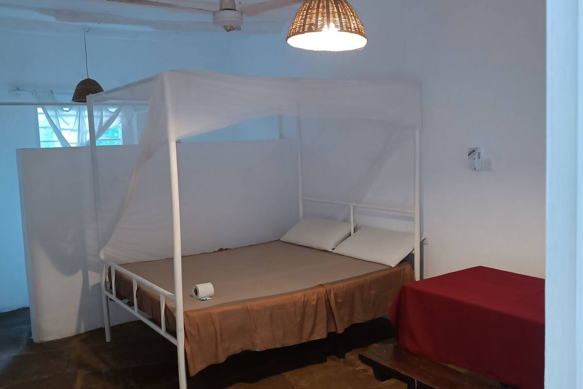 Una habitación con una cama individual, una litera, una mesa roja y una lámpara colgante.