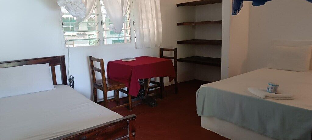 A room with two beds, a table with a red tablecloth, and a chair.