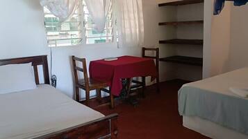 A room with two beds, a table with a red tablecloth, and a chair.