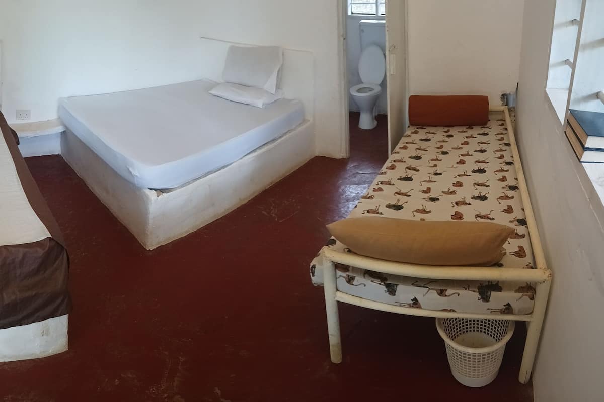 Una habitación pequeña y funcional con dos camas, una mesita y una ventana.