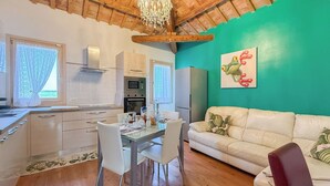 A modern kitchen with white cabinets, a dining table with chairs, a white sofa, and a green wall with a frog painting. - DAISY Luxury Apt in Villa, Patio, Pool, Hot Jacuzzi, A/C, WiFi, Gym, Sauna (SAN PIETRO DI CAVARZERE VENEZIA)