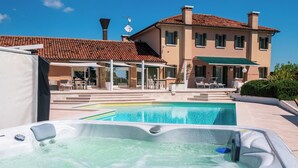 A swimming pool with a hot tub in the foreground, a covered patio area, and a two-story building with a tiled roof in the background. - DAISY Luxury Apt in Villa, Patio, Pool, Hot Jacuzzi, A/C, WiFi, Gym, Sauna (SAN PIETRO DI CAVARZERE VENEZIA)