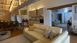 Un vaste espace de vie doté d’un haut plafond en bois, d’un canapé beige et d’un coin repas avec des chaises et une table.