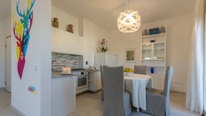 Cuina moderna amb zona de menjador, armaris blancs i un element decoratiu a la paret.