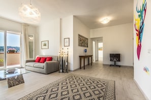 A spacious living room with a sofa, a patterned rug, a glass coffee table, and a modern pendant light.