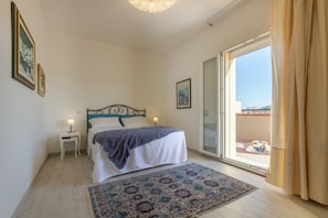 A bedroom with a bed, a nightstand, a window with curtains, and a view of the outside.