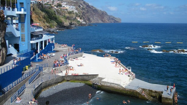 A coastal building with a pool area, a beach, and rocky cliffs in the background. - Charming OLD TOWN Penthouse W Large Private Sea Balcony  (Funchal)