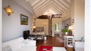 A cozy living room with a white sofa, a dining table, and a kitchen area with cabinets and a staircase. - Charming OLD TOWN Penthouse W Large Private Sea Balcony  (Funchal)