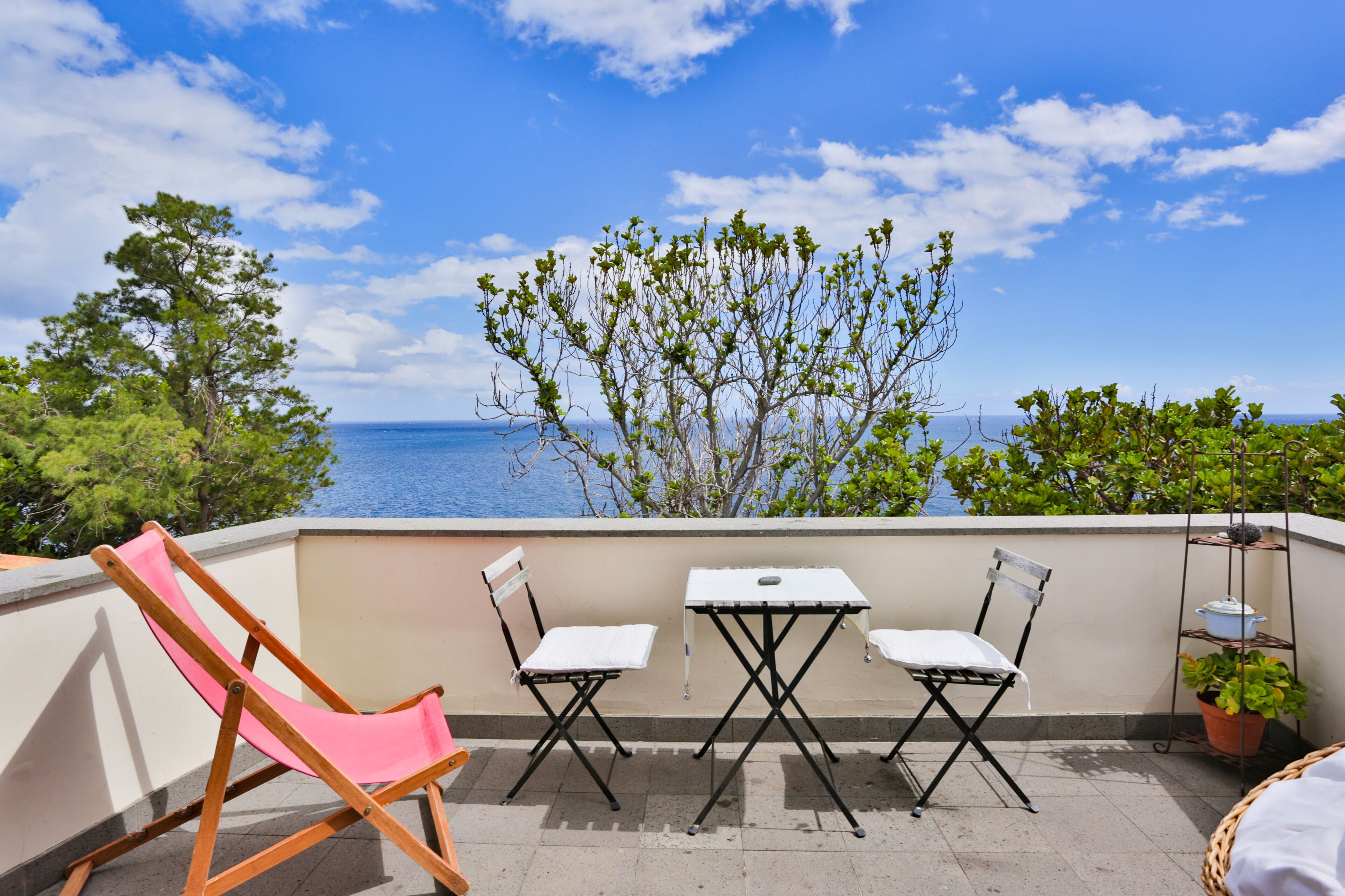 A balcony with a table and chairs, overlooking a body of water and greenery.