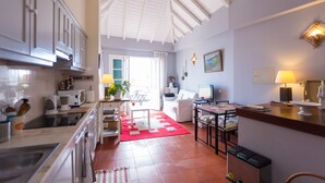 A spacious kitchen with modern appliances, a dining area with a red rug, and a living room with a white sofa and a TV. - Charming OLD TOWN Penthouse W Large Private Sea Balcony  (Funchal)