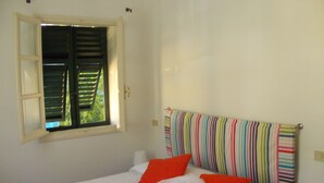 Een slaapkamer met een bed, een raam met luiken en een gestreept hoofdeinde.