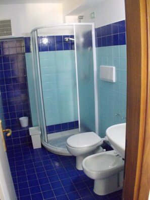 Un baño con azulejos azules, cabina de ducha de vidrio, dos inodoros y un lavabo.