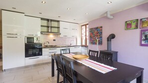 A modern kitchen with white cabinets, a stove, and a dining area with a table and chairs. -  House La Rosa "Bruno"    (Pian dei Manzi)