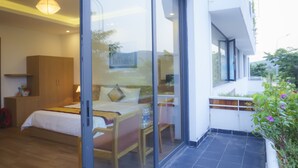Habitación de hotel moderna con cama, mesita de noche y puerta de cristal que da a un balcón con vistas al exterior.