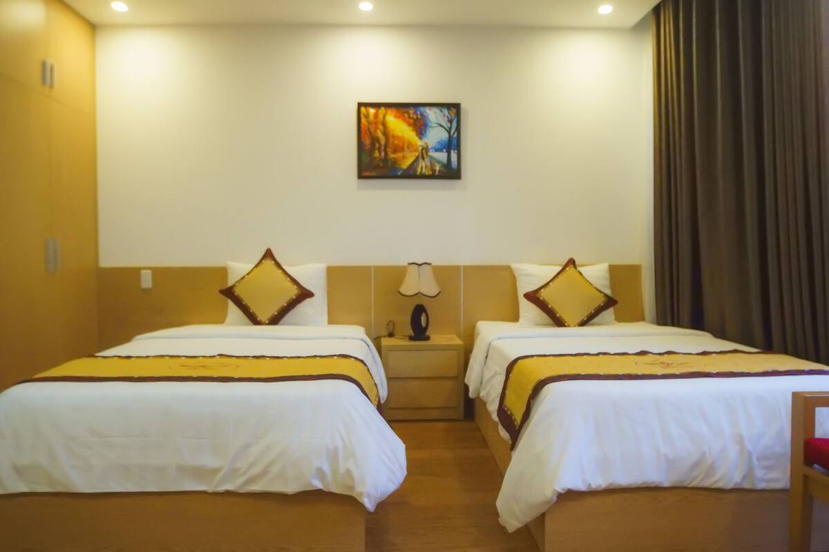 A hotel room with two beds, a nightstand with a lamp, and a painting on the wall.