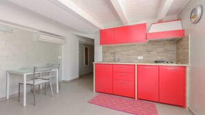 A compact kitchen with red cabinets, a glass dining table, and a pink rug.
