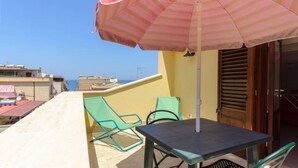 A balcony with a table and two chairs, an umbrella, and a view of the sea.
