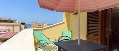 A balcony with a table and two chairs, an umbrella, and a view of the sea.