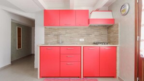 A compact kitchen with red cabinets, a tiled backsplash, and a small countertop.