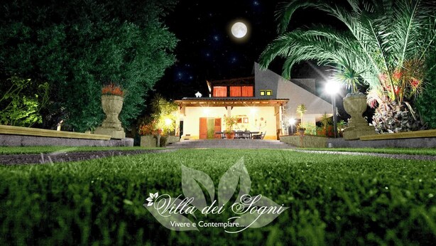 Vue nocturne de la Villa dei Soani, avec une entrée bien éclairée, un patio et une végétation luxuriante.