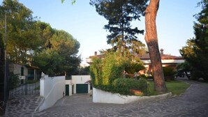 Un camino pavimentado que conduce a una entrada con puerta de reja, un muro blanco y un pequeño jardín.