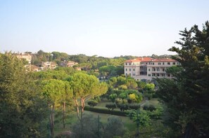 A large, multi-story building with a red roof, surrounded by lush greenery and trees. - Rome: Apartment in gated community, close to the center of Rome (Roma)