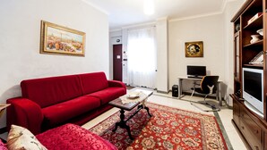 Una sala de estar con un sofá rojo, una mesa de centro, un televisor y una estantería.
