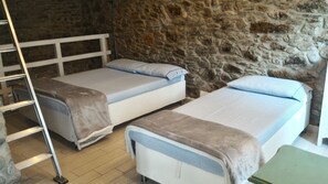 Une chambre avec deux lits simples, une échelle en bois et un mur en pierre.