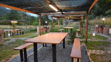 An outdoor patio area with wooden tables and benches, surrounded by a gravel path and greenery.