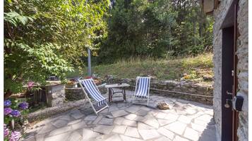 Een terras met stenen vloer, twee gestreepte lounge fauteuils en een kleine tafel.