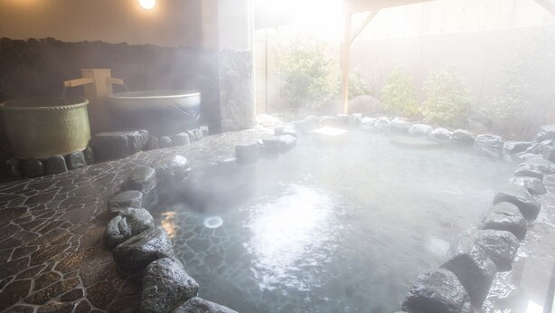 A hot spring bath area with stone flooring, a stone wall, and a wooden structure.