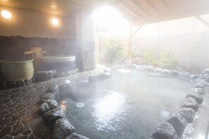 A hot spring bath area with stone flooring, a stone wall, and a wooden structure. - Sun Plaza Hotel Fuji Lake Yamanaka (Yamanakako)