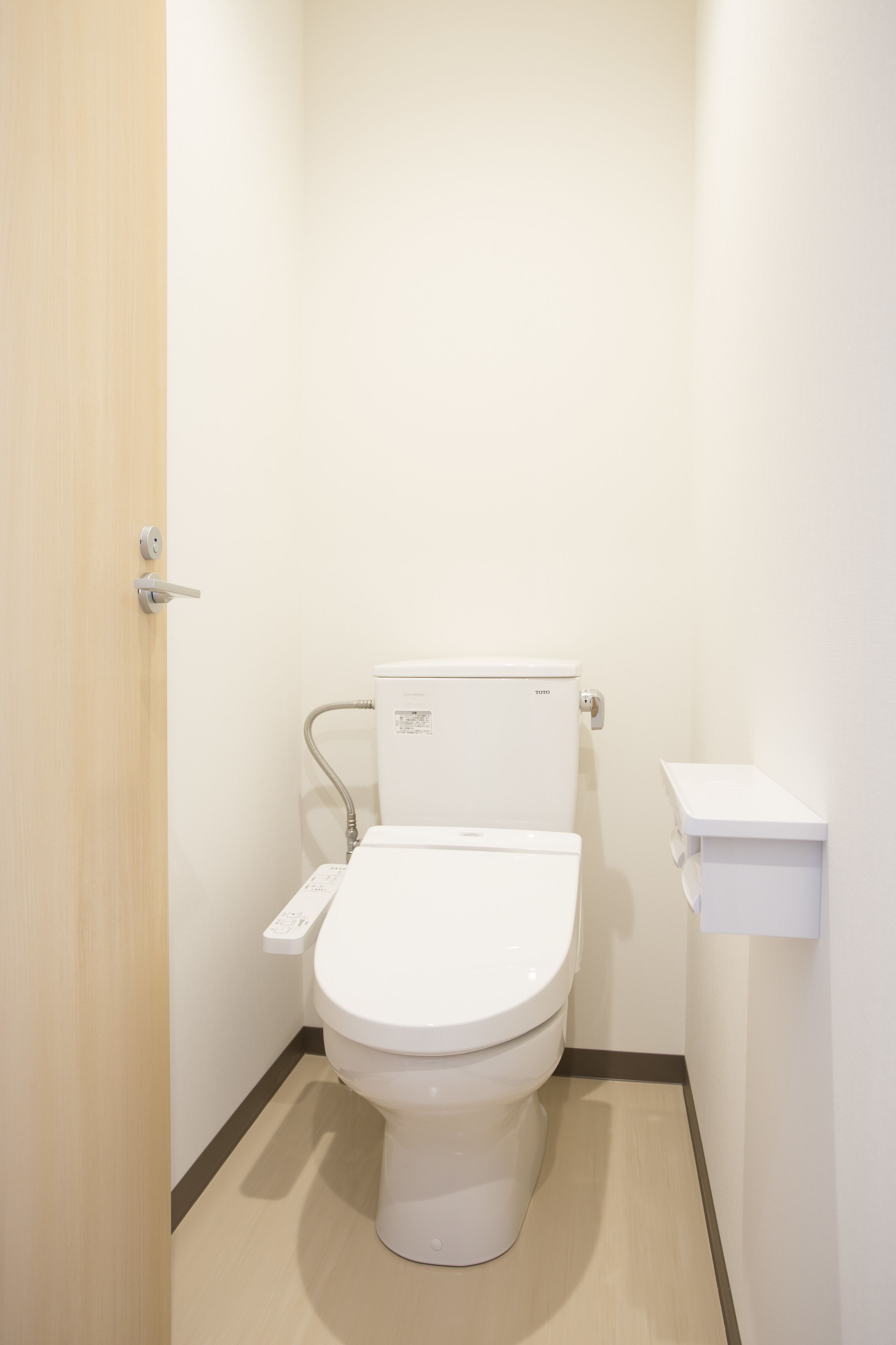 Un baño pequeño y limpio con inodoro, dispensador de papel higiénico y lavamanos instalado en la pared.