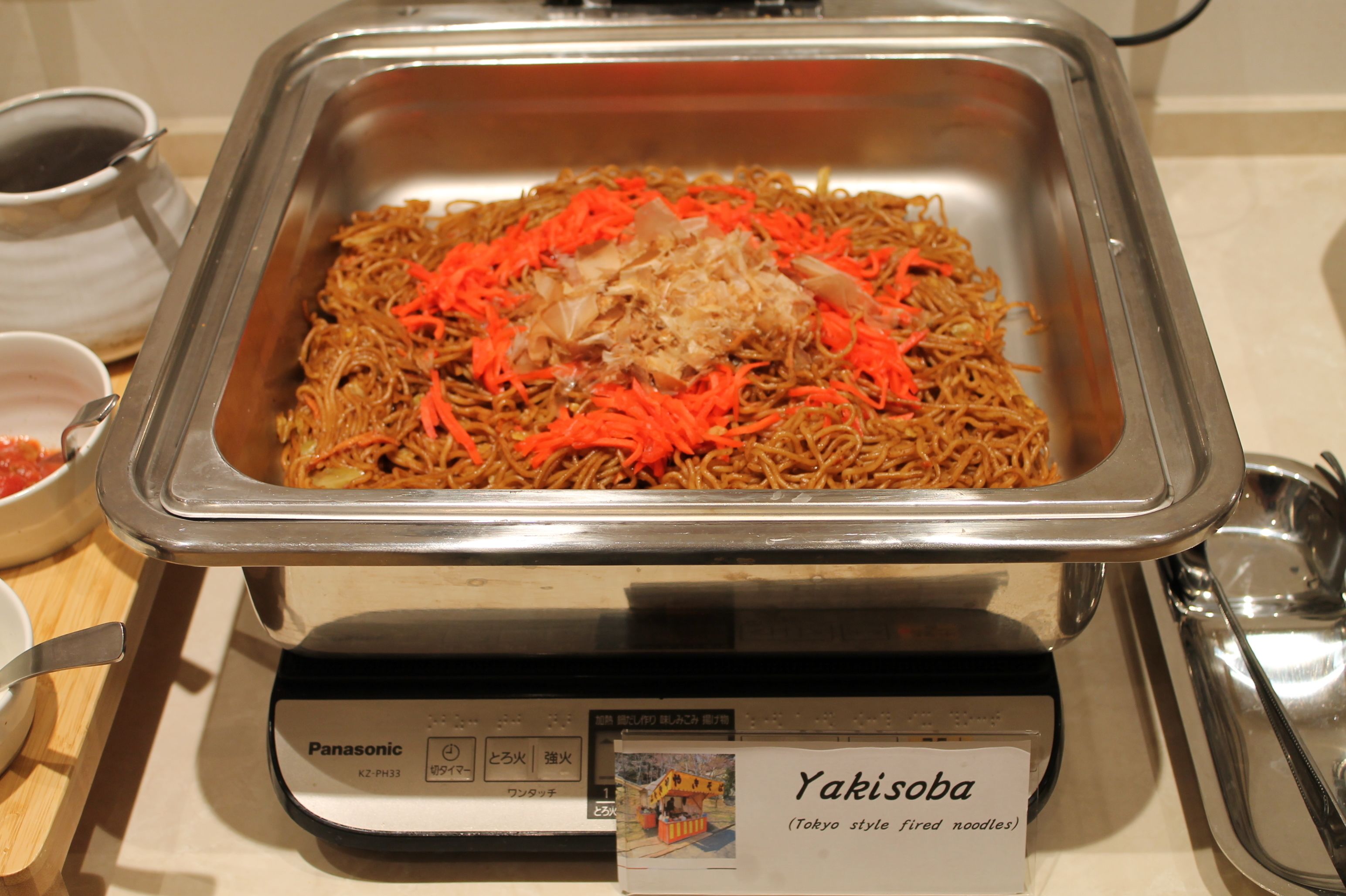 Un bufé con una variedad de platos, incluyendo un plato de Yakisoba señalizado.