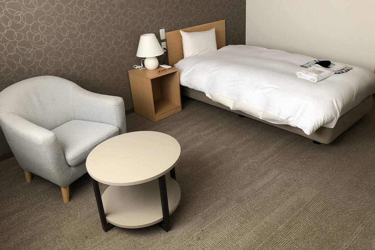 A compact hotel room with a single bed, a small table, and a chair.