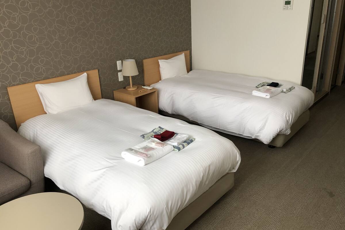 A hotel room with two beds, a sofa, a round table, and a lamp.