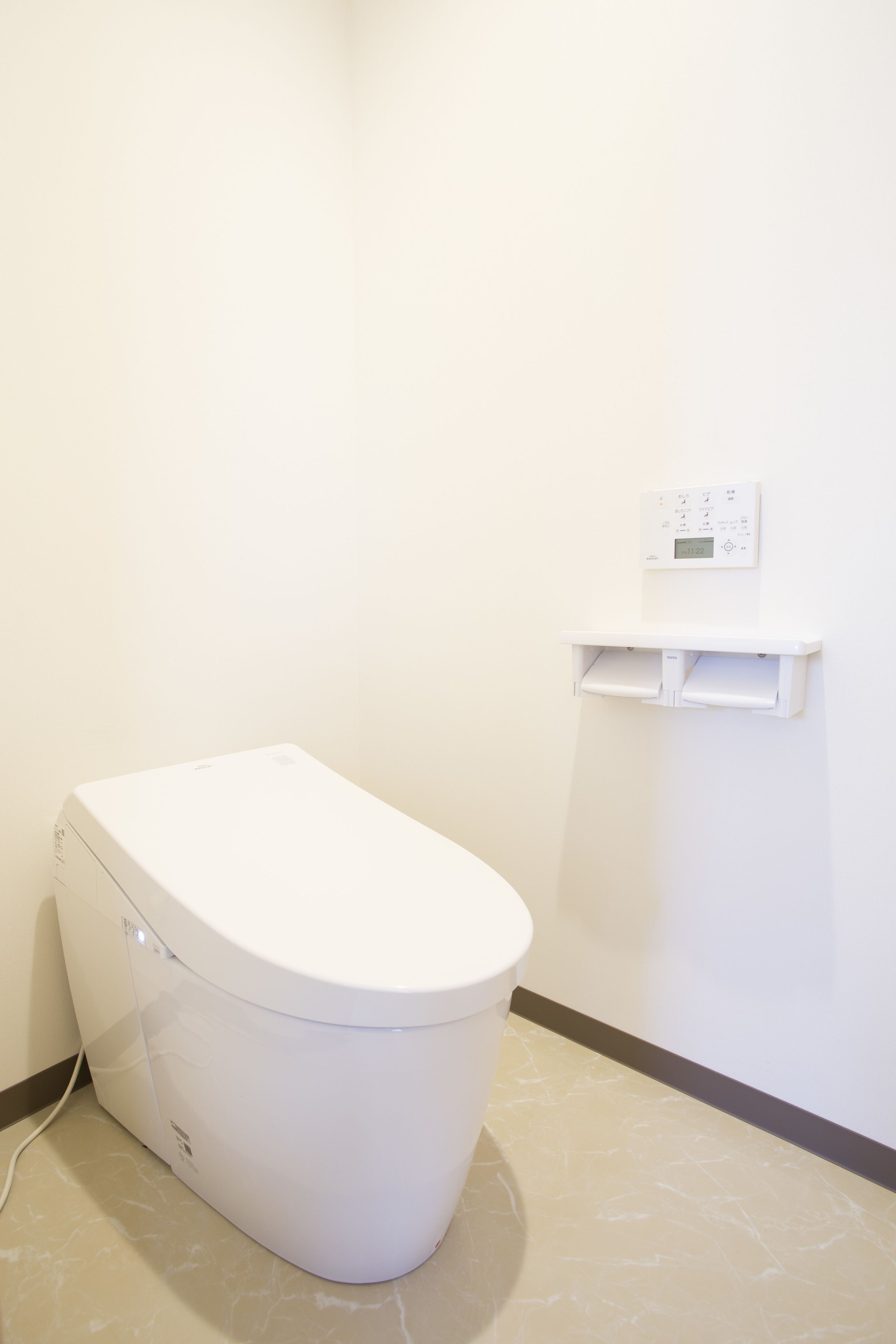 A white toilet with a control panel above it, a white shelf below, and a tiled floor.