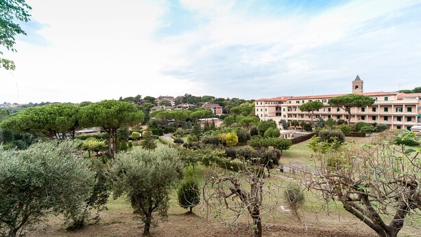 A view of a residential area with a large building with a tower, surrounded by well-maintained gardens and trees. - COTTAGE cozy and comfortable (Roma)